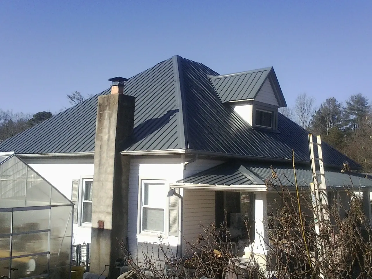 Dark blue standing seam metal roof on a white farmhouse with dormer — Slate & Tile Roof Repair by Roofing Brothers in Dunbar