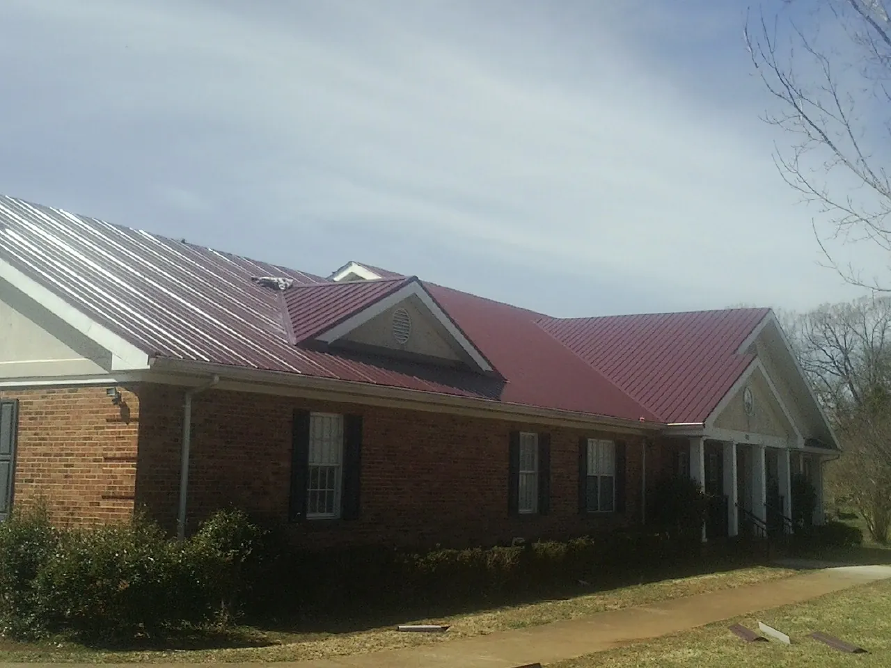 Red metal roof with gabled entries on a long brick building, from a Hail Damage Roof Repair job in Dunbar