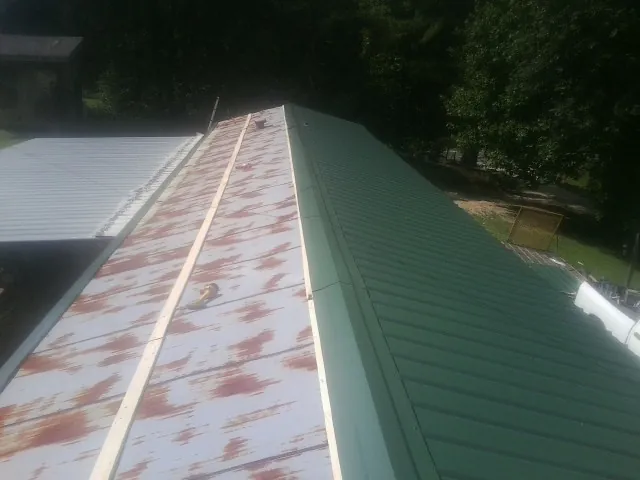 Old rusted panels beside newly installed green metal roofing — Wind Damage Roof Repair by Roofing Brothers in Dunbar