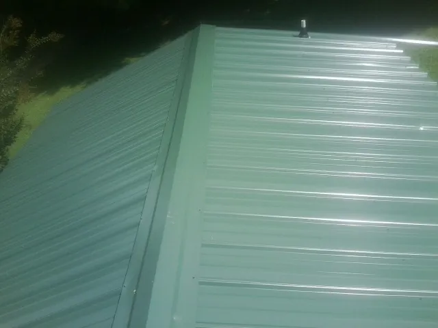 New green metal panels meeting at the ridge of a roof — Flat Roof Repair work by our crew in Dunbar