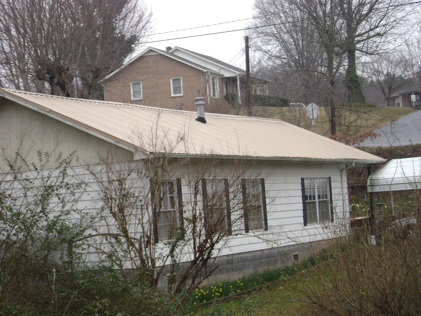 Tan metal roof on a white sided house set into a hillside — Commercial Roofing by Roofing Brothers in Dunbar
