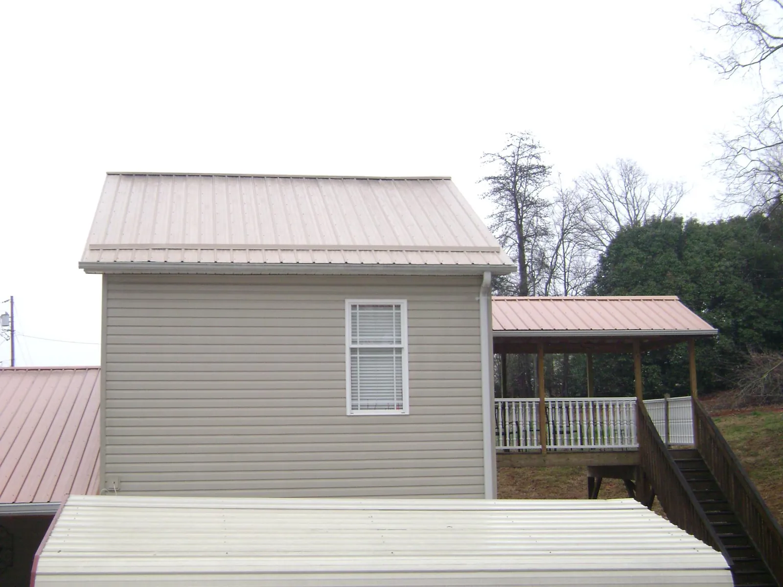 Tan metal roofs on a two story addition and attached porch, from a Roof Replacement job in Dunbar